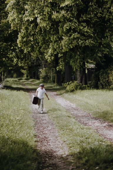 Ein Kind geht auf einem schmalen Weg durch eine grüne, bewaldete Landschaft.