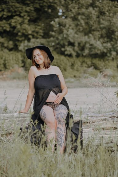 Frau mit Sommerkleid und Hut sitzt im Grünen, umgeben von Natur.