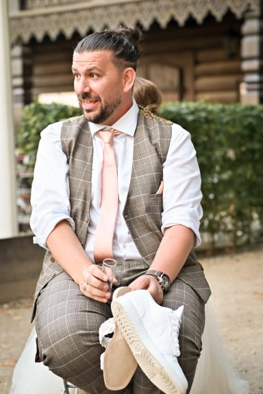 Mann in Anzug mit Krawatte sitzt und hält einen weißen Schuh in der Hand.