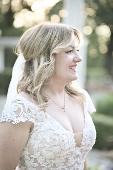 Braut in einem weißen Kleid mit langen blonden Haaren und schlichten Accessoires.